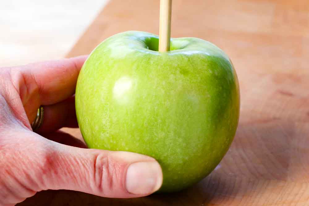 showing how to make caramel apples by sticking a an apple stick into the center core of the apple