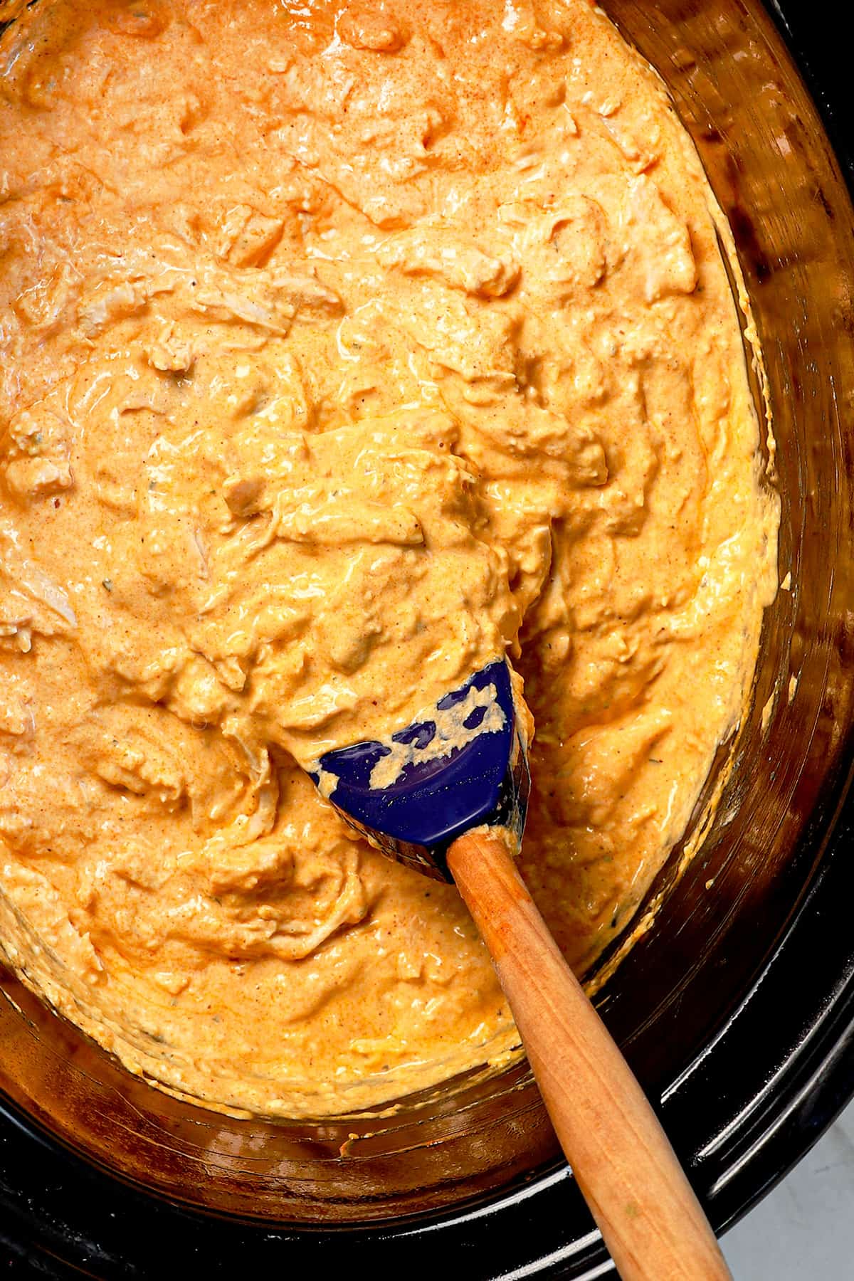 showing how to make crockpot buffalo dip by cooking until the crream cheese and cheese are melted, then stirring to combine and showing how creamy it is