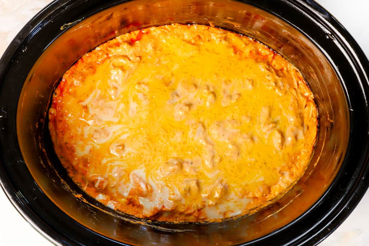 showing how to make crockpot buffalo chicken dip by melting cheese over top of the dip
