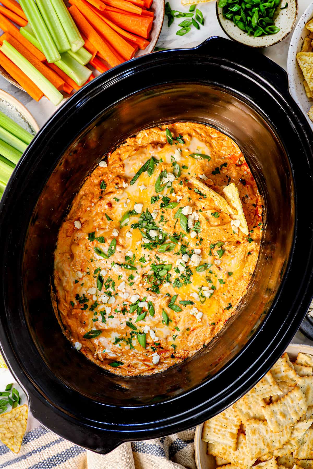 showing how to serve crockpot buffalo chicken dip chicken surrounded by celery, carrots, crackers and chips