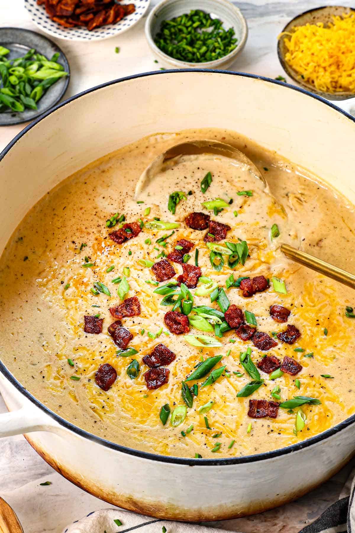loaded baked potato soup in a pot topped with green onions, bacon and cheese