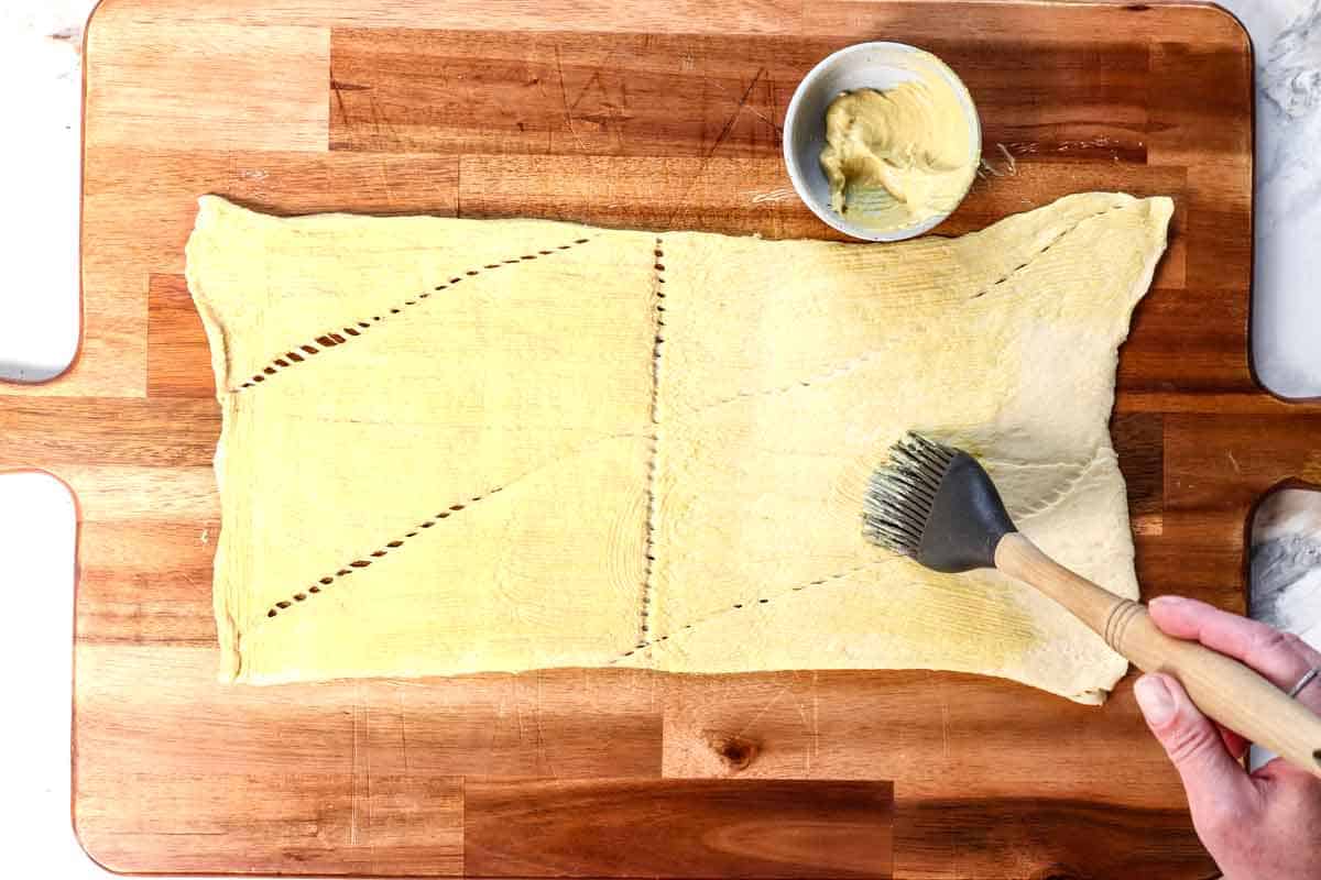 showing how to make Pigs in a Blanket buy brushing the crescent rolls with Dijon mustard