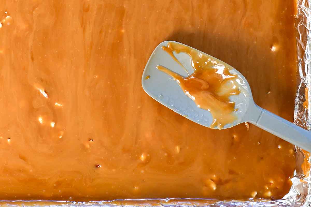 showing how to make almond roca by spreading the toffee over the chopped almonds