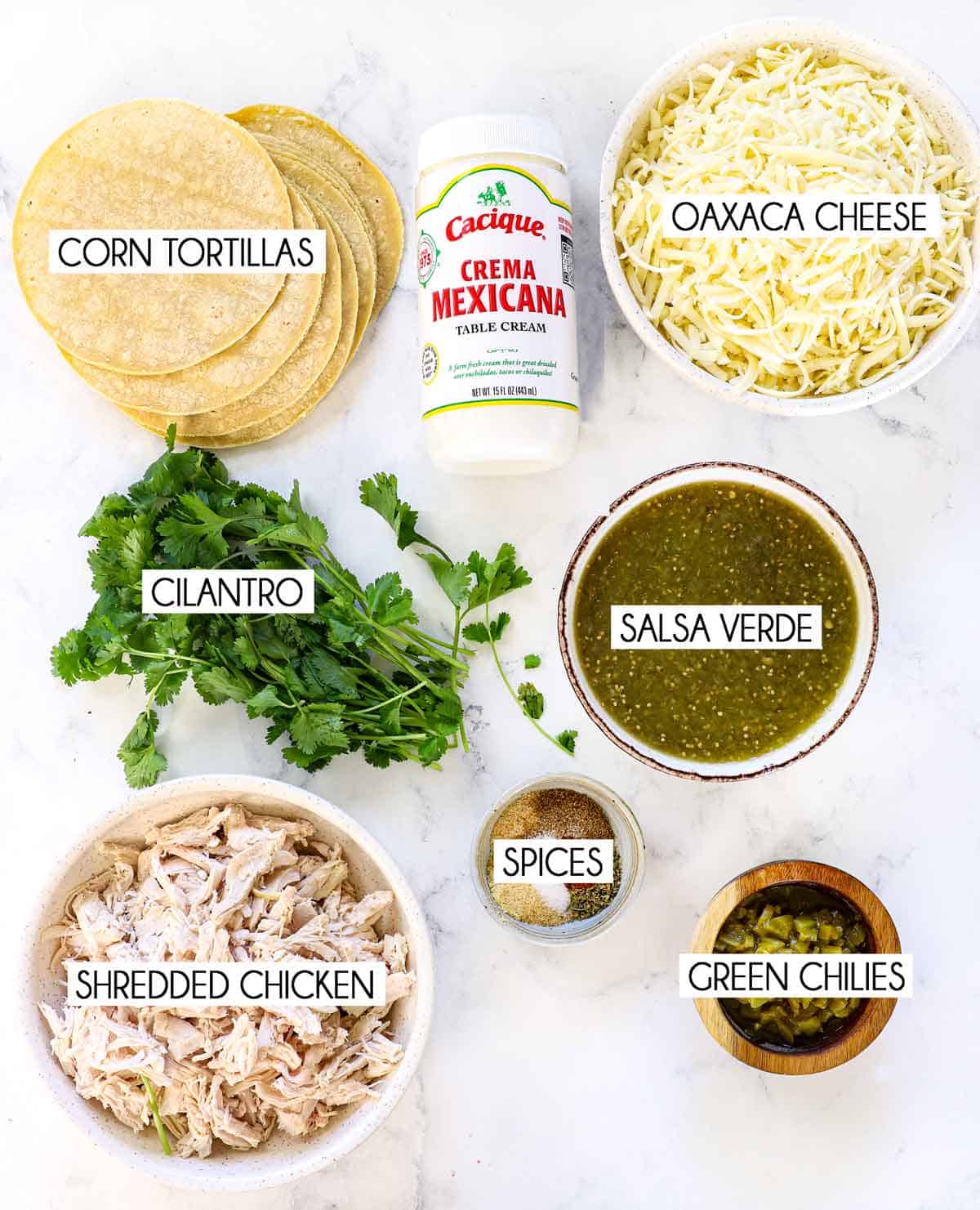 top view of enchiladas suizas ingredients: shredded chicken, corn tortillas Oaxaca cheese, salsa verde, cilantro and Mexican crema