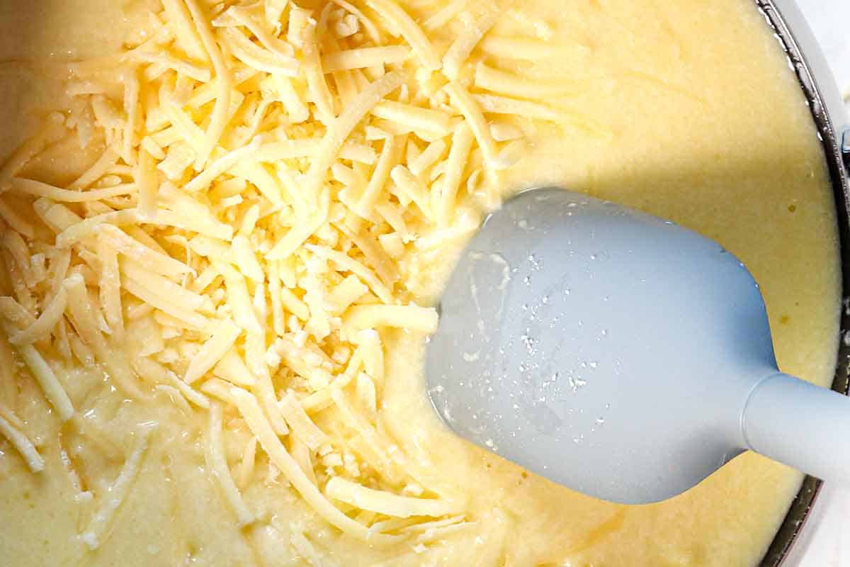 showing how to make cheese fondue by adding the cheeses a handful at a time and stirring in between each addition to melt