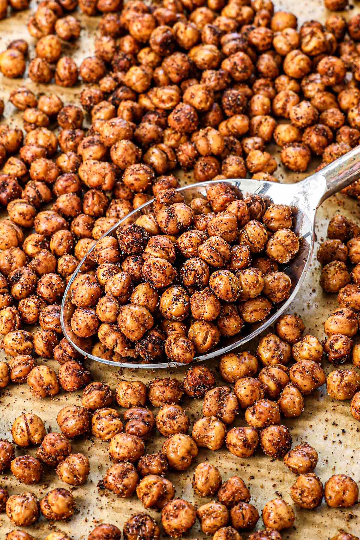 up close of roasted chickpeas recipe on a baking sheet being scooped by a spoon showing the spices