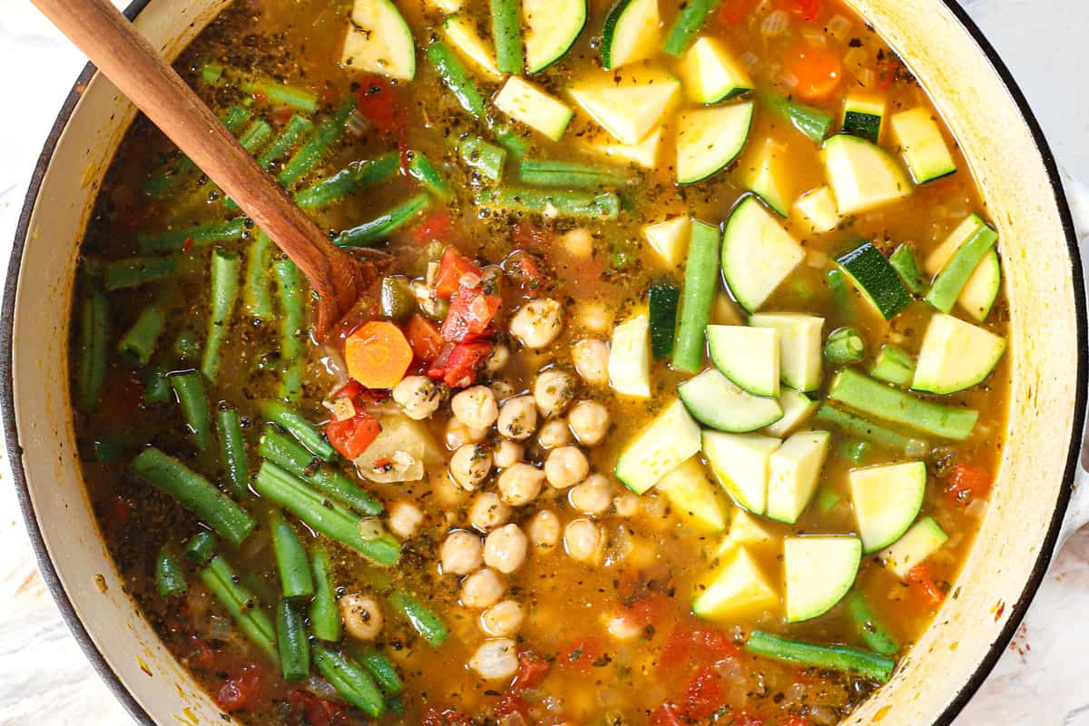 showing how to make vegetable soup by adding chickpeas, green beans, and zucchini and simmeirng