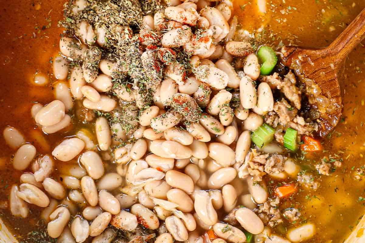 showing how to make white bean soup by adding white beans, spices and broth to the soup and simmering