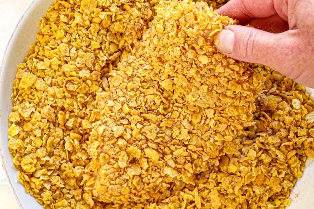 showing how to make hot honey chicken by dredging the chicken in the cornflakes to coat