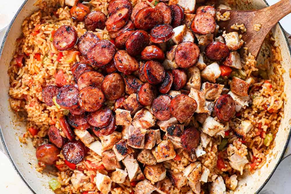 showing how to make jambalaya by adding the chicken, sausage and shrimp back to the rice