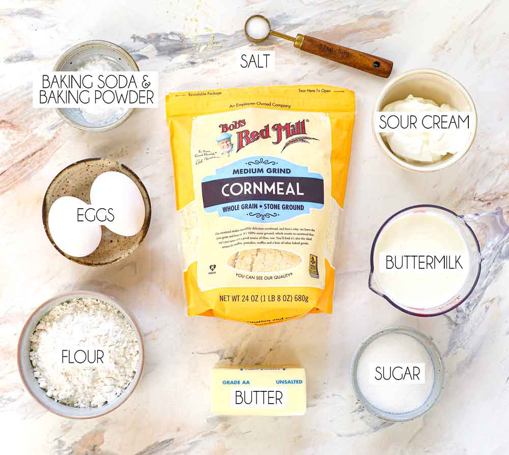 top view of skillet cornbread recipe ingredients: medium grind cornmeal, flour, baking powder, baking soda, sour cream, butter, sugar, salt