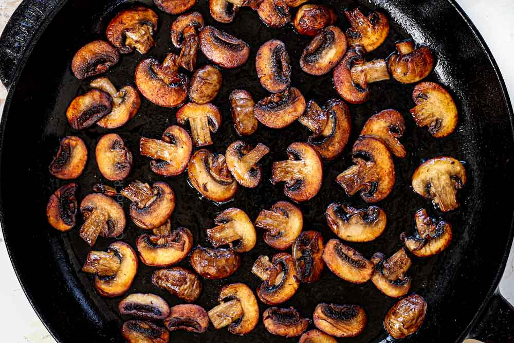 showing how to make smothered pork chops by caramelizing the mushrooms in a cast iron skillet