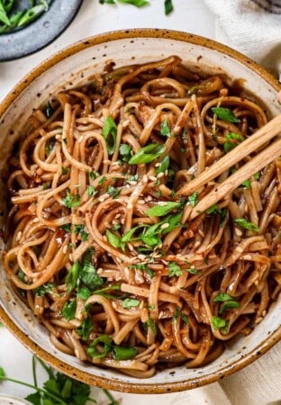 top view of spicy noodles with chili oil in a bowl being eaten with chopsticks