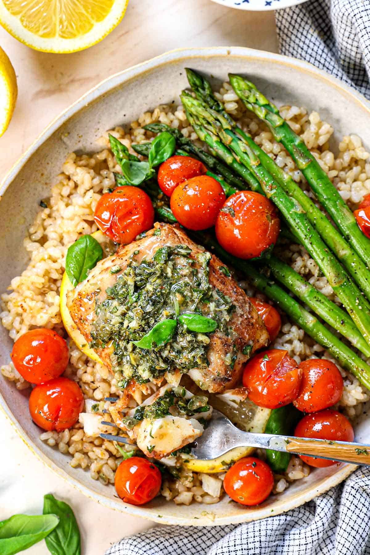 top view of showing how to served baked cod fish on a plate with rice, asparagus and tomatoes