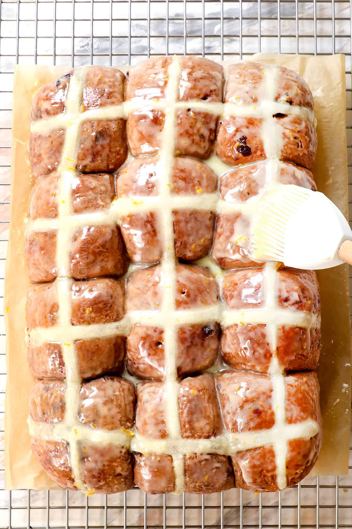 showing how to make hot cross buns with a top shot of brushing the glaze over the top of the buns