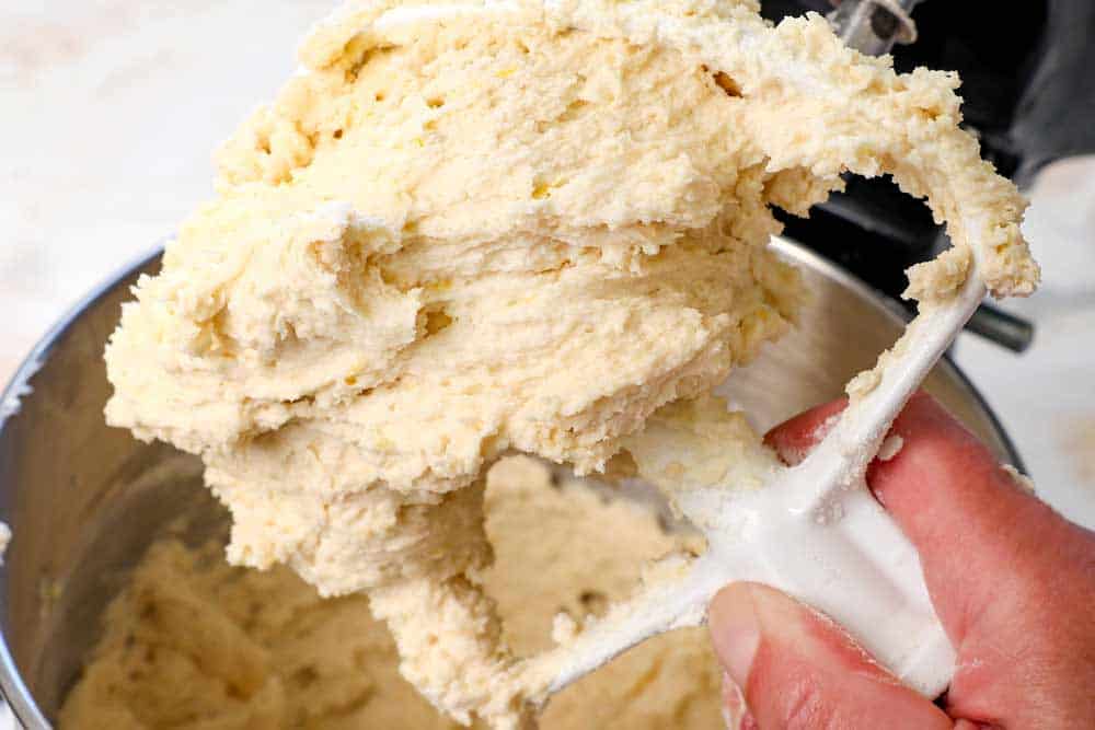 showing how to make lemon cookies by holding up the mixer paddle attachment showing the consistency of the cookie dough