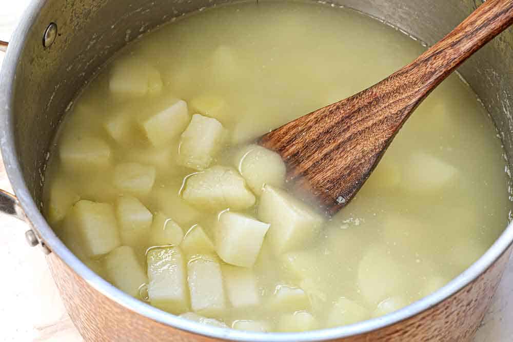 showing how to make mashed potato casserole by boiling the chunks of potatoes in water