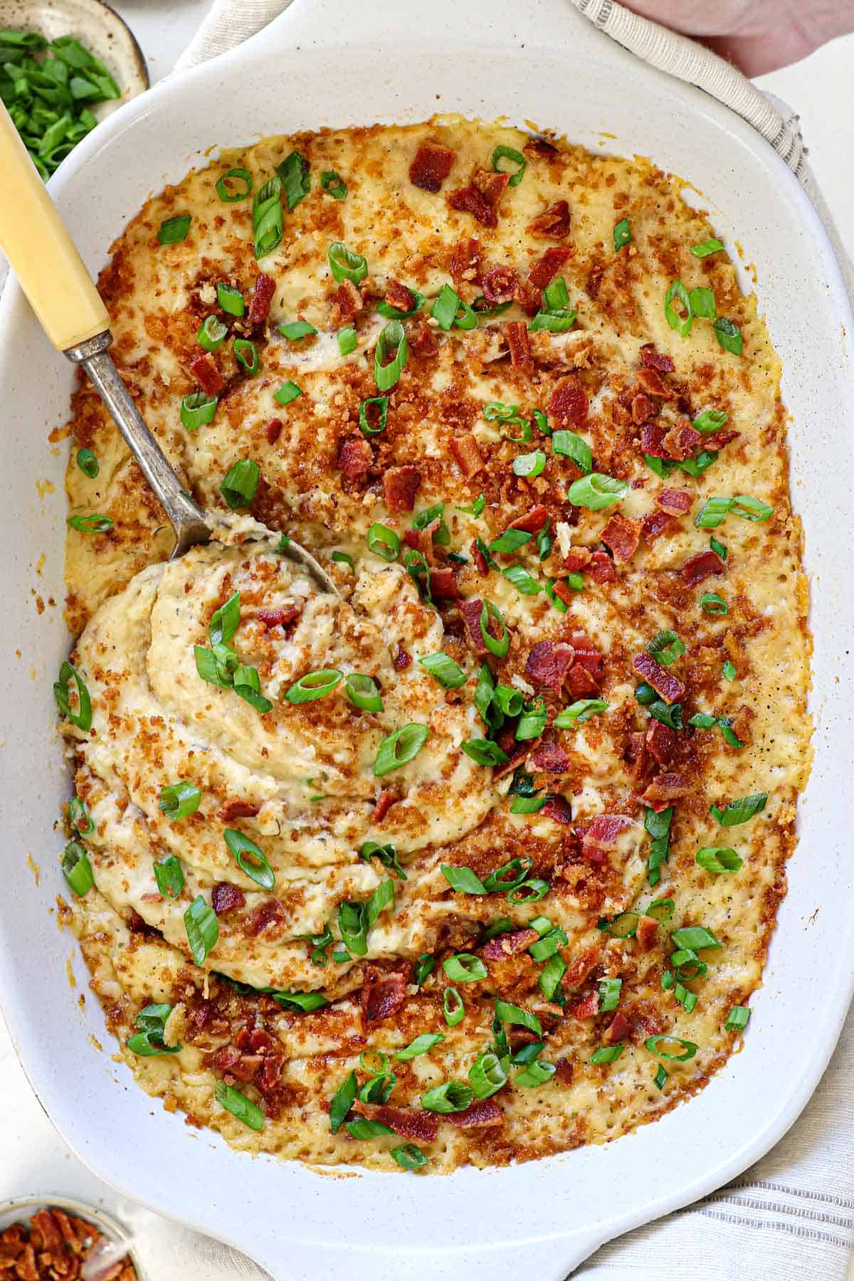 top view of holding mashed potato casserole recipe showing the panko topping, cheeses, bacon and, green onions