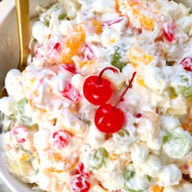 top view of ambrosia salad being served in a bowl with mandarin oranges, maraschino cherries, pineapple tidbits, grapes, marshmallows and coconut