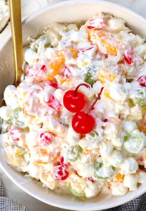 top view of ambrosia salad being served in a bowl with mandarin oranges, maraschino cherries, pineapple tidbits, grapes, marshmallows and coconut