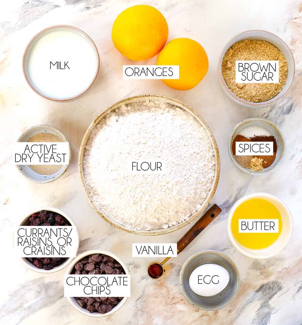 top view of hot cross buns ingredients: flour, active dry yeast, brown sugar, cinnamon, nutmeg, cloves, melted butter, egg, vanilla, dried cranberries (or raisins, or currants), vanilla, chocolate chips