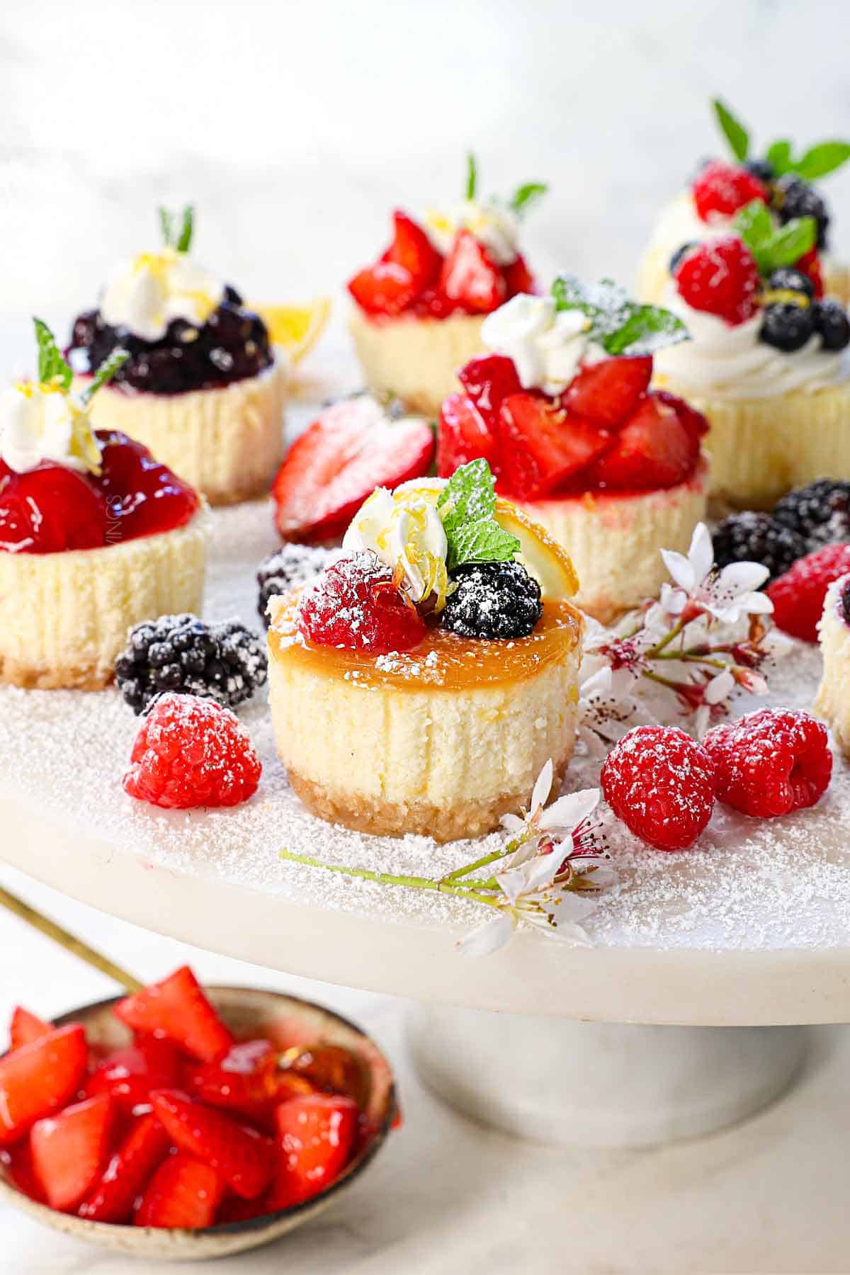 mini cheesecakes recipe topped with lemon curd, strawberries, blueberries, whipped cream and caramel sauce