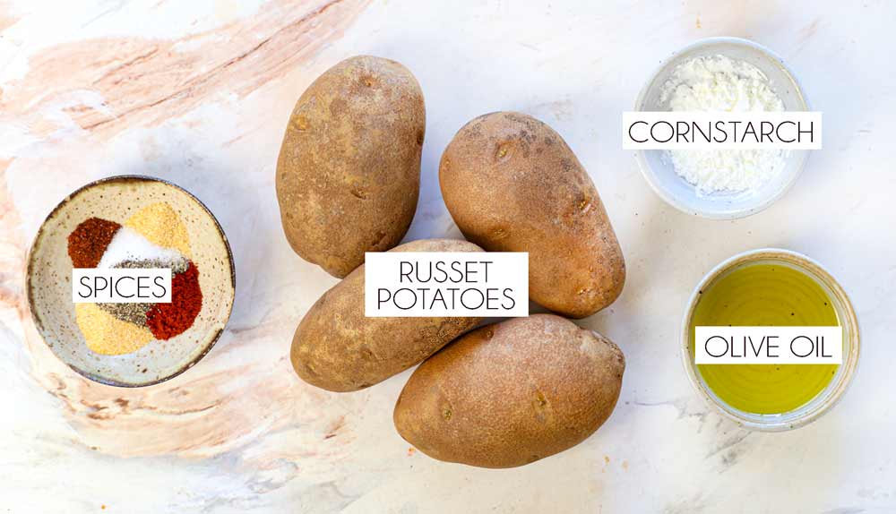 top view of potato wedges ingredients: Russet potatoes, cornstarch, olive oil, smoked paprika, onion powder, garlic powder, salt, pepper