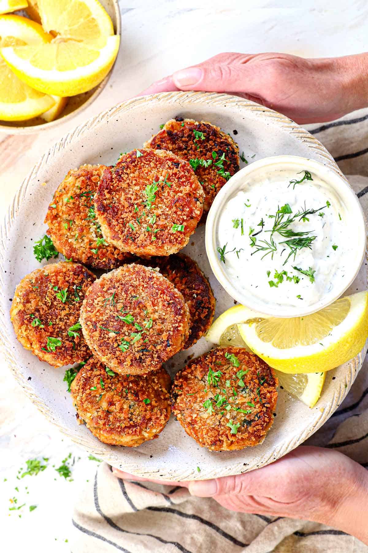 showing how to serve fried salmon croquettes croquettes by holding a plate with dip and lemons